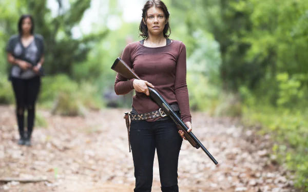 Maggie Greene, portrayed by Lauren Cohan, stands confidently with a rifle in a wooded setting from the TV show The Walking Dead. A dramatic scene in HD wallpaper format.
