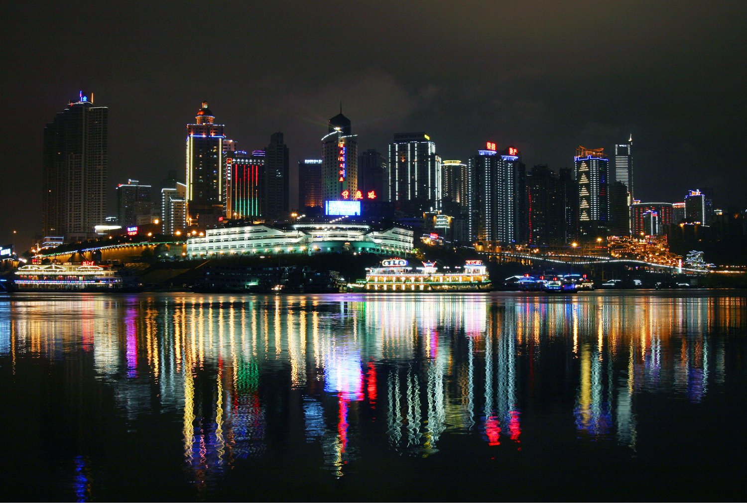 HD desktop wallpaper showcasing a city skyline at night with vibrant lights reflecting on calm water, highlighting man-made architectural beauty.