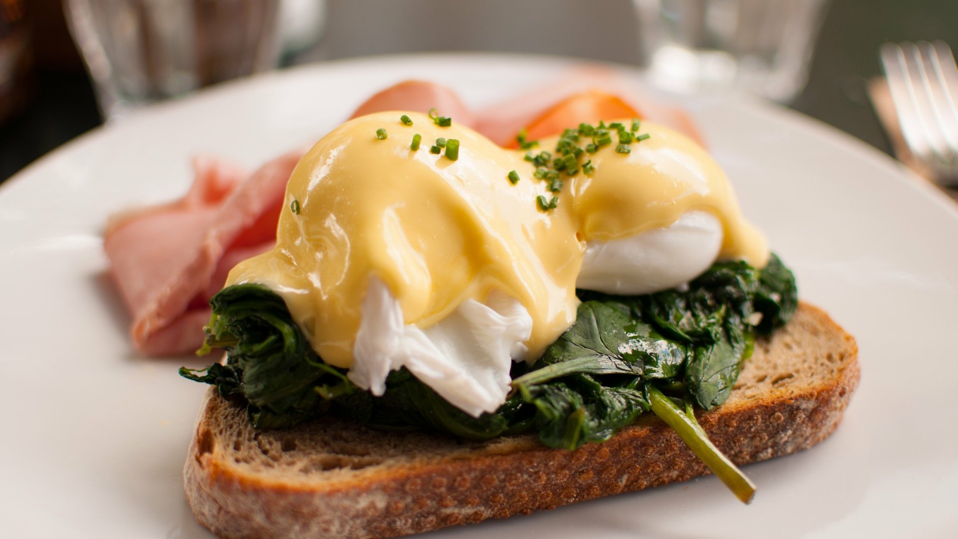 Close-up of a breakfast meal featuring toast topped with sautéed spinach, poached eggs, and hollandaise sauce, captured in 4K Ultra HD for a vibrant PC desktop wallpaper.
