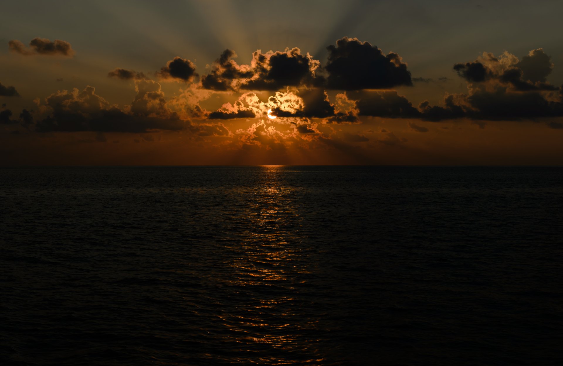 4K Ultra HD PC desktop wallpaper and background: sunset over the ocean horizon, sun piercing clouds with golden sunbeams reflecting on the water — a serene nature scene.