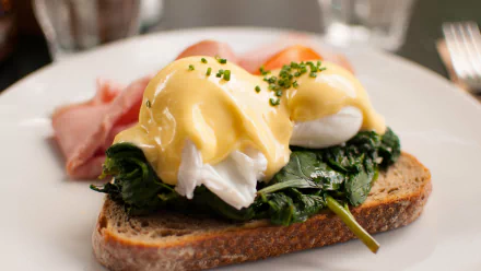 Close-up of a breakfast meal featuring toast topped with sautéed spinach, poached eggs, and hollandaise sauce, captured in 4K Ultra HD for a vibrant PC desktop wallpaper.