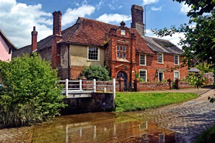 2K Quad HD PC desktop wallpaper and background: man-made historic brick house by a calm canal with a white footbridge, cobblestone path and lush greenery under a blue sky.