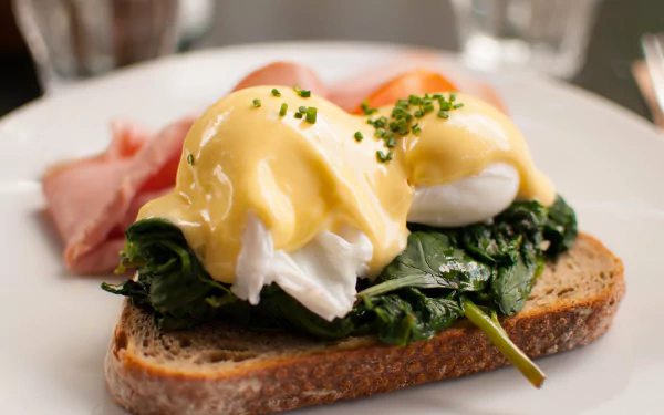 Close-up of a breakfast meal featuring toast topped with sautéed spinach, poached eggs, and hollandaise sauce, captured in 4K Ultra HD for a vibrant PC desktop wallpaper.