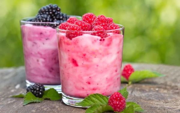 A 4K UHD desktop wallpaper featuring creamy yogurt desserts topped with fresh raspberries and blackberries, styled as a vibrant berry milkshake on a rustic wooden surface.