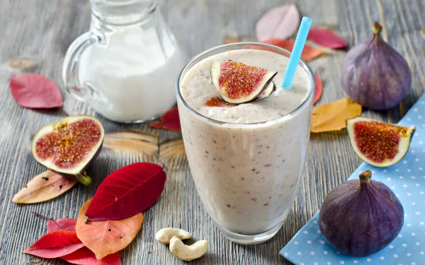 A refreshing smoothie topped with fig slices, surrounded by colorful autumn leaves, and a jug of milk, set against a wooden backdrop. Vibrant and inviting food-themed wallpaper.
