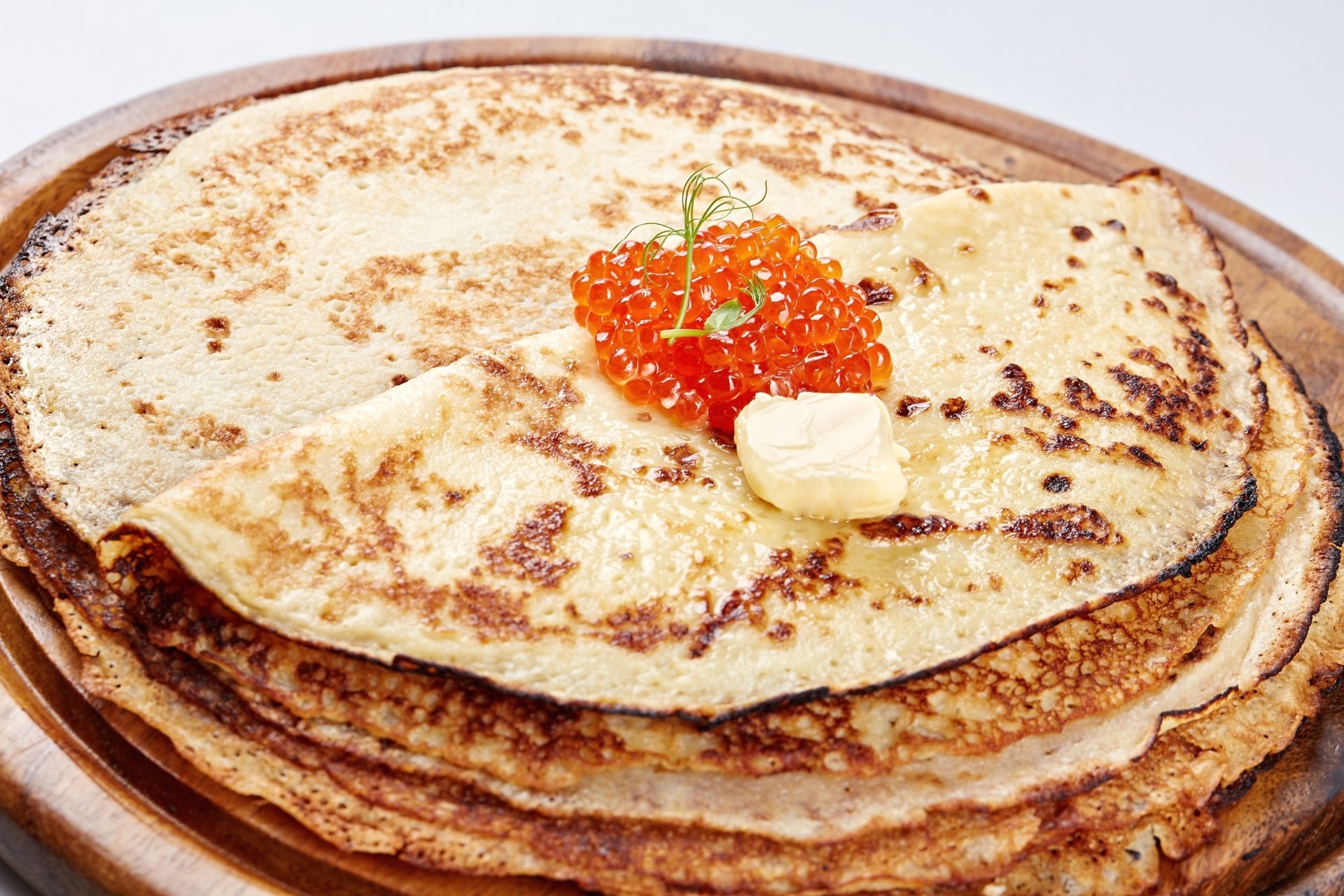 A stack of golden crêpes topped with a dollop of butter and vibrant orange caviar, captured in sharp 4K Ultra HD detail for a rich food wallpaper background.