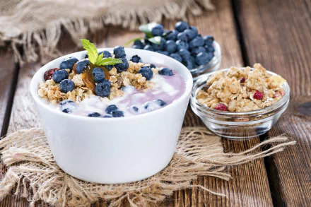 A 4K Ultra HD desktop wallpaper showing a bowl of blueberry yogurt topped with granola and fresh berries, set on a rustic wooden surface.