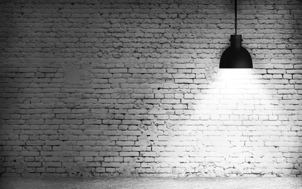 A high-definition desktop wallpaper featuring a textured brick wall illuminated by a hanging black lamp, creating a moody and atmospheric setting.