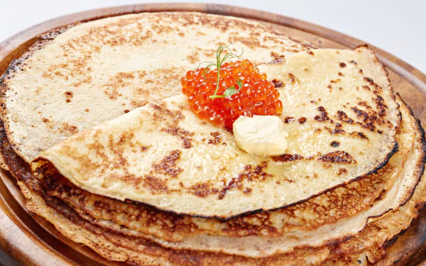 A stack of golden crêpes topped with a dollop of butter and vibrant orange caviar, captured in sharp 4K Ultra HD detail for a rich food wallpaper background.
