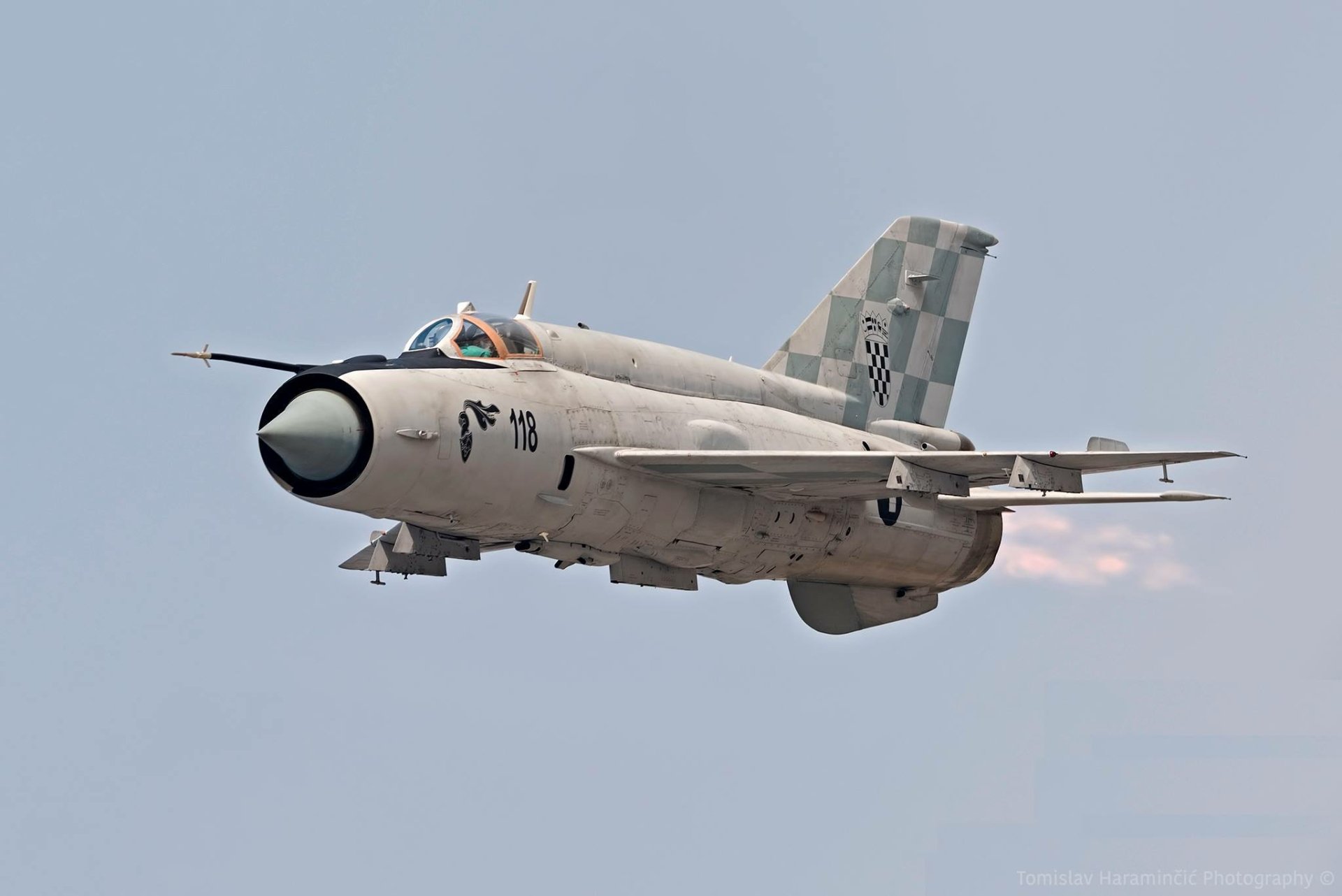 HD desktop wallpaper featuring a Mikoyan-Gurevich MiG-21 military jet in flight against a clear sky background.