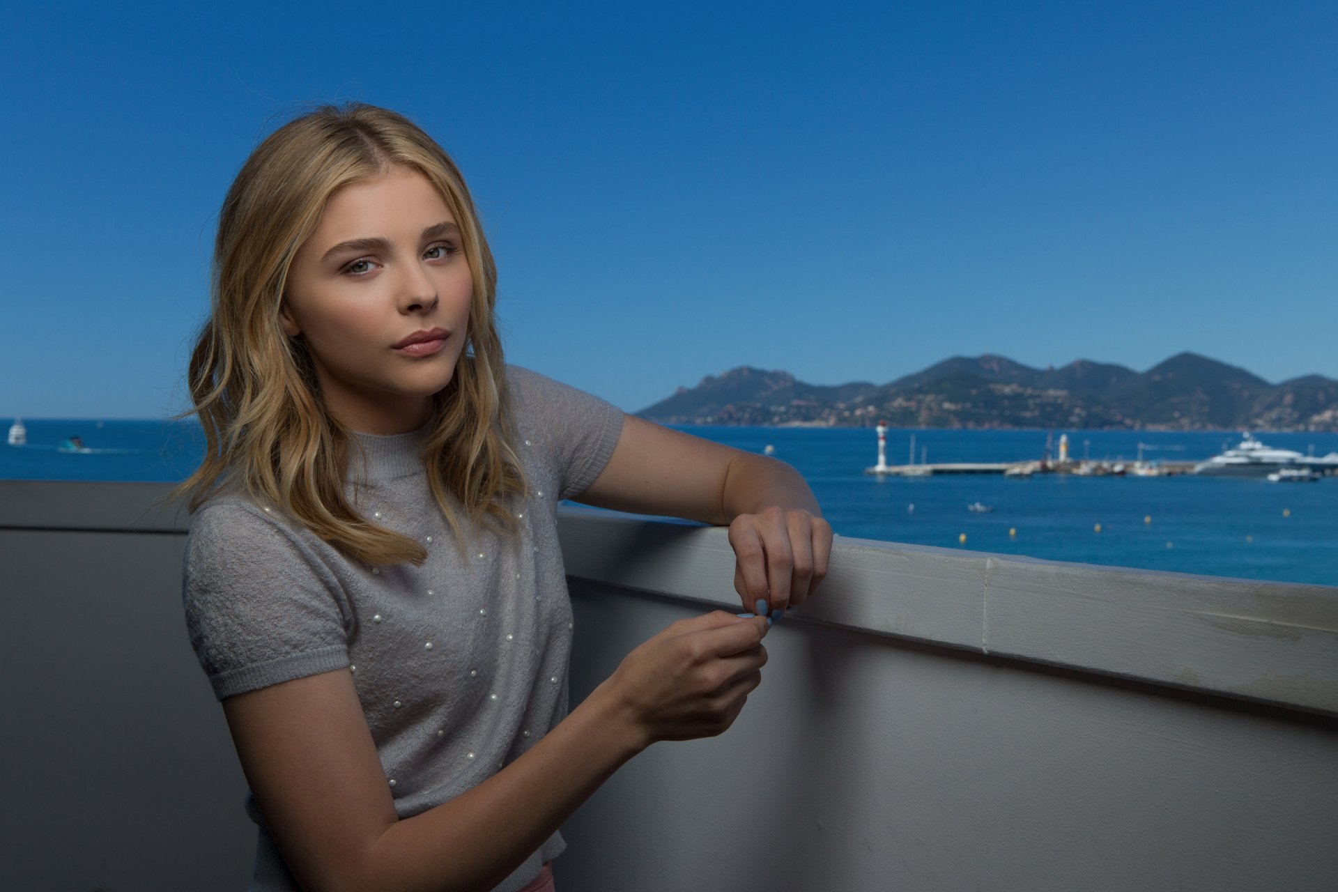 Chloë Grace Moretz poses thoughtfully against a stunning coastal backdrop, captured in a vibrant 4K Ultra HD image, showcasing her style and poise.