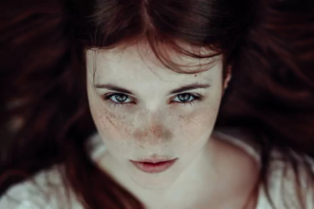 A striking HD desktop wallpaper featuring a woman with freckles, gazing directly at the viewer, surrounded by flowing hair that enhances her captivating look.