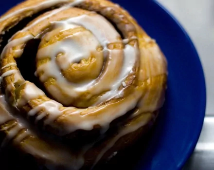 A close-up of a delicious cinnamon roll drizzled with icing, displayed on a blue plate. This HD desktop wallpaper captures the enticing allure of sweet treats.