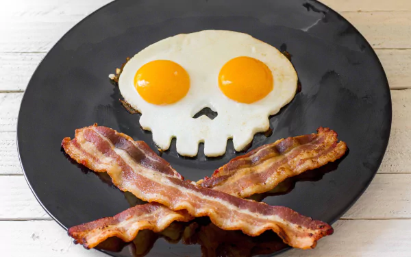 HD desktop wallpaper showing a breakfast plate with two fried eggs shaped like a skull and crossed strips of crispy bacon forming a pirate-style design.