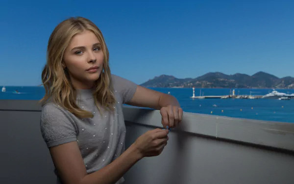 Chloë Grace Moretz poses thoughtfully against a stunning coastal backdrop, captured in a vibrant 4K Ultra HD image, showcasing her style and poise.