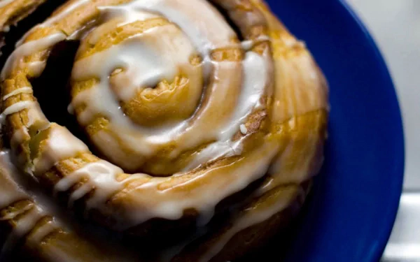 A close-up of a delicious cinnamon roll drizzled with icing, displayed on a blue plate. This HD desktop wallpaper captures the enticing allure of sweet treats.