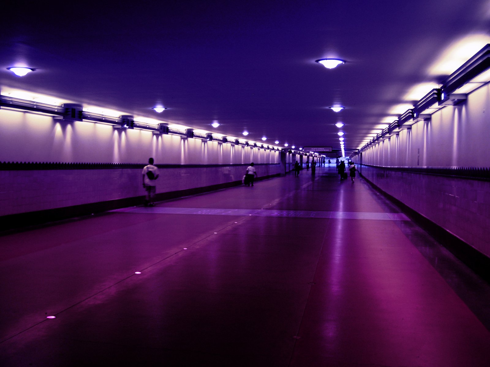 HD PC desktop wallpaper of a man-made tunnel with purple lighting, showcasing a long, illuminated walkway with a few people walking inside.