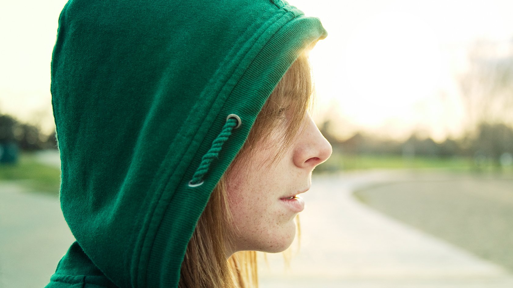 HD PC desktop wallpaper featuring a close-up profile of a woman wearing a green hoodie, with soft natural light highlighting her face against a blurred outdoor background.