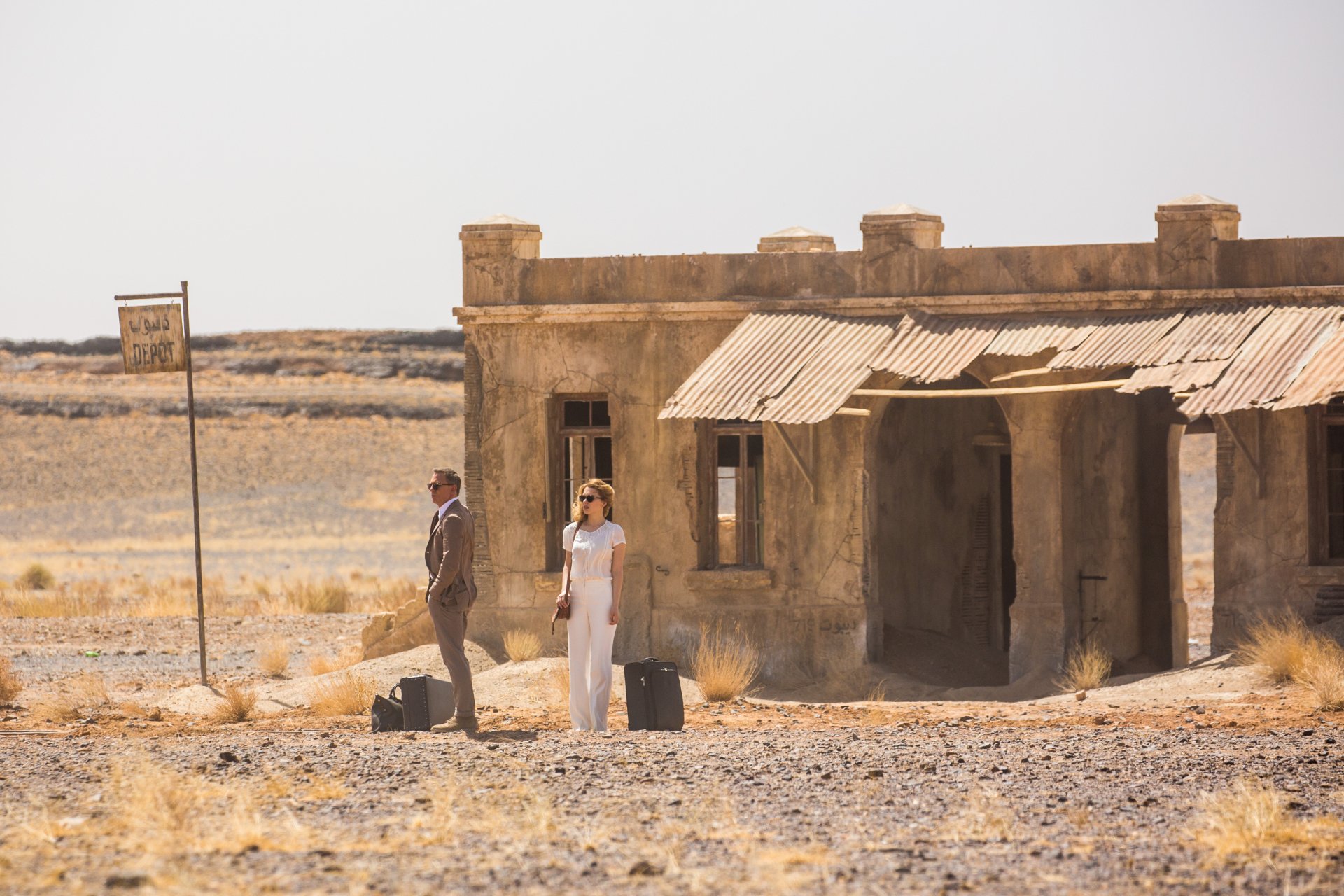 Léa Seydoux as Madeleine Swann and Daniel Craig as James Bond stand outside a weathered building in a desolate landscape from the movie Spectre. A cinematic moment captured in 4K Ultra HD.