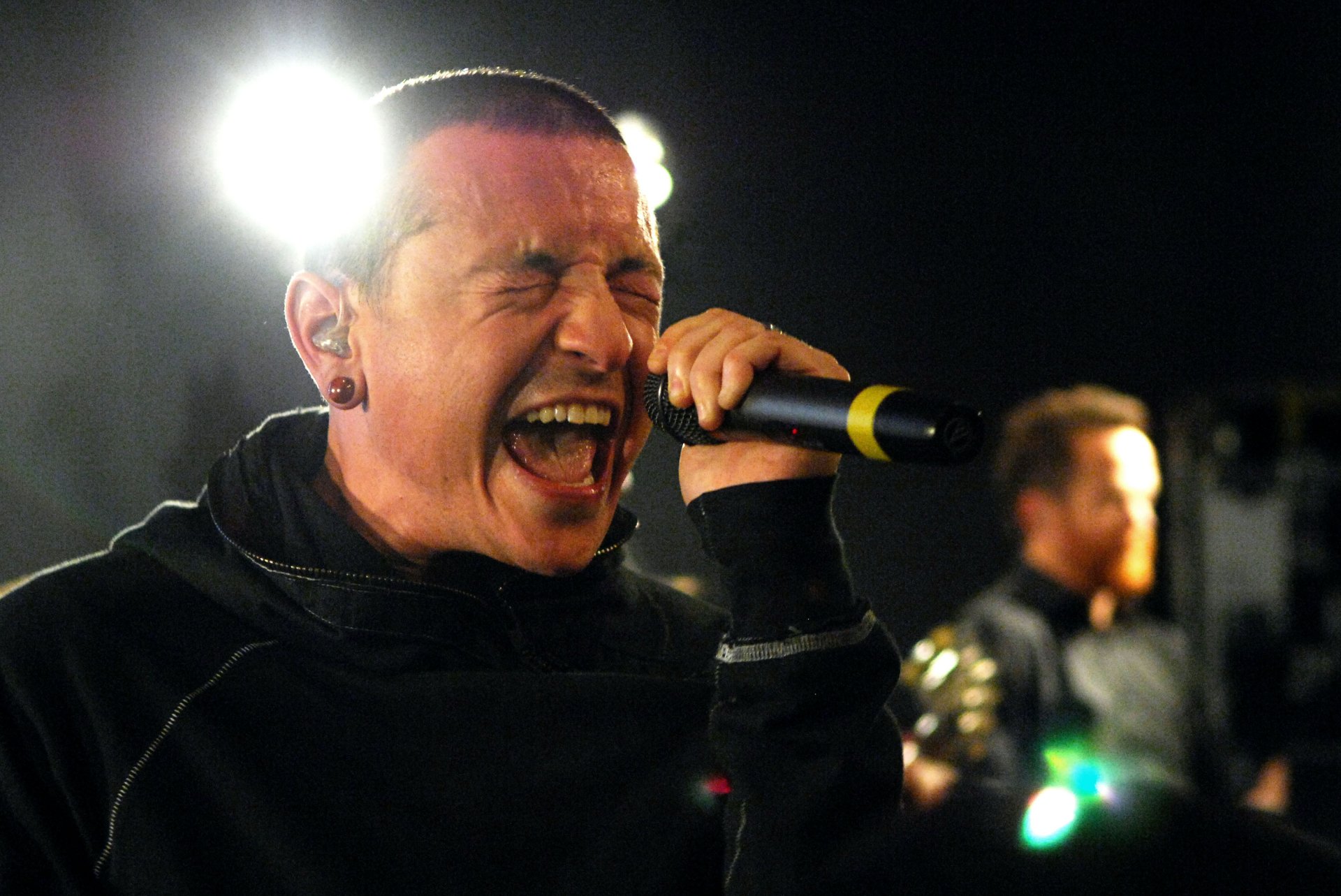 A high-definition desktop wallpaper featuring a powerful performance by Linkin Park's lead vocalist, passionately singing into a microphone under bright stage lights.