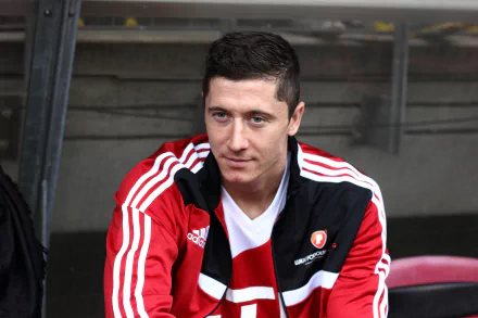 HD wallpaper of Polish soccer player Robert Lewandowski, dressed in a red and white sports jacket, sitting and gazing off-camera.
