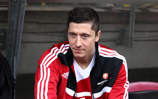 HD wallpaper of Polish soccer player Robert Lewandowski, dressed in a red and white sports jacket, sitting and gazing off-camera.