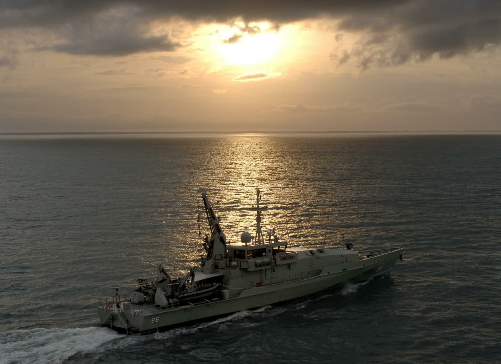 HMAS Glenelg (ACPB 96), a Royal Australian Navy patrol boat/warship, steaming across calm sea at sunset — HD PC desktop wallpaper.