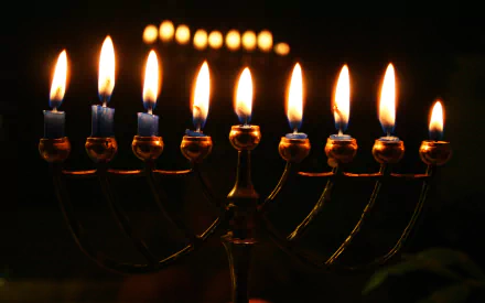 HD PC desktop wallpaper featuring a brightly lit Hanukkah menorah with nine glowing candles against a dark background, celebrating the holiday of Hanukkah.