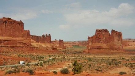 HD PC desktop wallpaper featuring the rugged red rock formations and expansive desert landscape of Arches National Park under a partly cloudy sky.