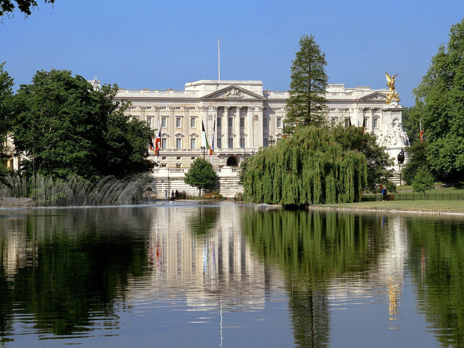 A striking HD wallpaper featuring a grand palace surrounded by lush greenery, reflecting beautifully in a calm body of water under a clear blue sky.