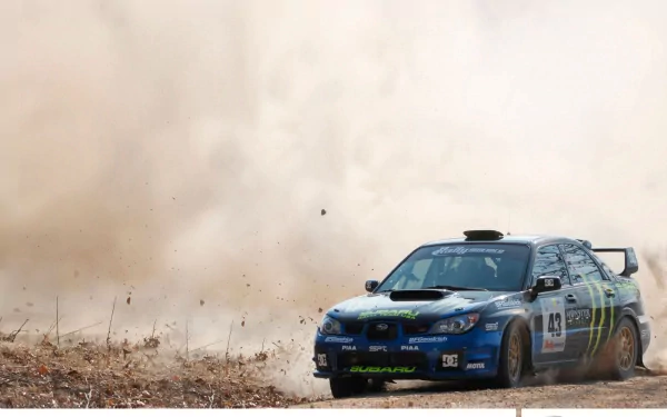 A rally car, blue with green accents, speeds through a dusty landscape, kicking up dirt and debris, captured in an HD desktop wallpaper.