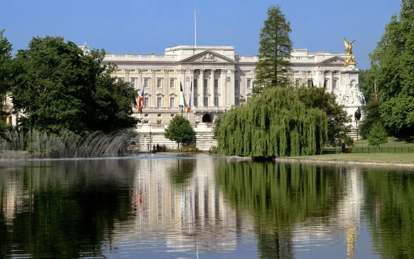 A striking HD wallpaper featuring a grand palace surrounded by lush greenery, reflecting beautifully in a calm body of water under a clear blue sky.