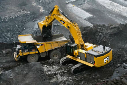 HD desktop wallpaper featuring a yellow Caterpillar vehicle operating in a construction site, with an excavator loading dirt into a dump truck.