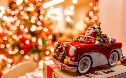 HD holiday Christmas desktop wallpaper featuring a miniature red vintage car filled with festive decorations against a warm, blurred background of twinkling lights.