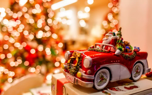 HD holiday Christmas desktop wallpaper featuring a miniature red vintage car filled with festive decorations against a warm, blurred background of twinkling lights.