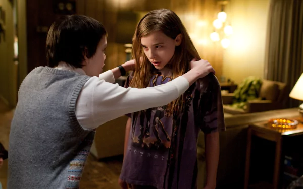 Chloë Grace Moretz stars in a scene from the movie Let Me In, capturing a tense moment between characters in a dimly lit room, creating a haunting atmosphere.