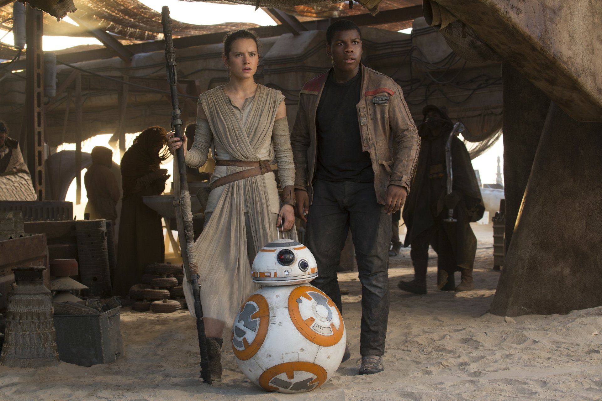 Rey and Finn stand together in a sandy setting, with BB-8 beside them, in a scene from Star Wars Episode VII: The Force Awakens. High-definition wallpaper capturing this dynamic trio.