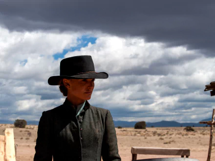 HD desktop wallpaper featuring Natalie Portman in character from the movie Jane Got a Gun, set against a vast desert landscape under a cloudy sky.