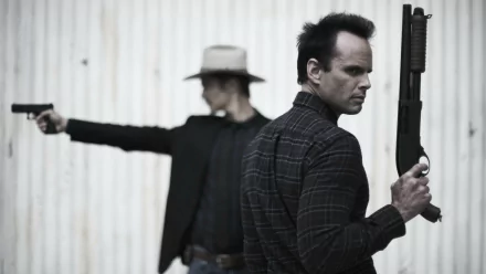 HD PC wallpaper from TV show Justified: two armed men back-to-back, one holding a shotgun and the other in a cowboy hat aiming a pistol against a corrugated metal wall.