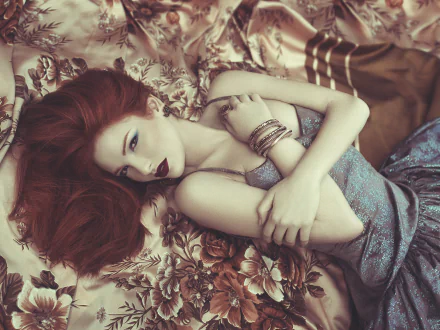 HD wallpaper of a redhead woman model lying down in a dress, wearing jewelry, and bold lipstick, set against a floral patterned background.