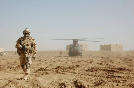 A soldier walks on dusty terrain with a Boeing CH-47 Chinook military helicopter hovering in the background, captured in HD for a PC desktop wallpaper.