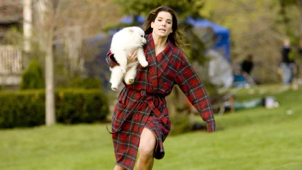 Sandra Bullock as Margaret Tate runs in a plaid robe, carrying a dog in a scene from the movie The Proposal. This HD image captures a moment of humor and spontaneity.
