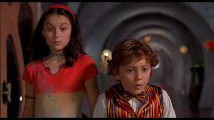 HD PC desktop wallpaper: two children in colorful outfits stand in a dim arched corridor with surprised expressions — scene from the movie Spy Kids.