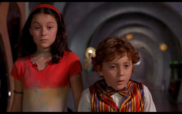 HD PC desktop wallpaper: two children in colorful outfits stand in a dim arched corridor with surprised expressions — scene from the movie Spy Kids.