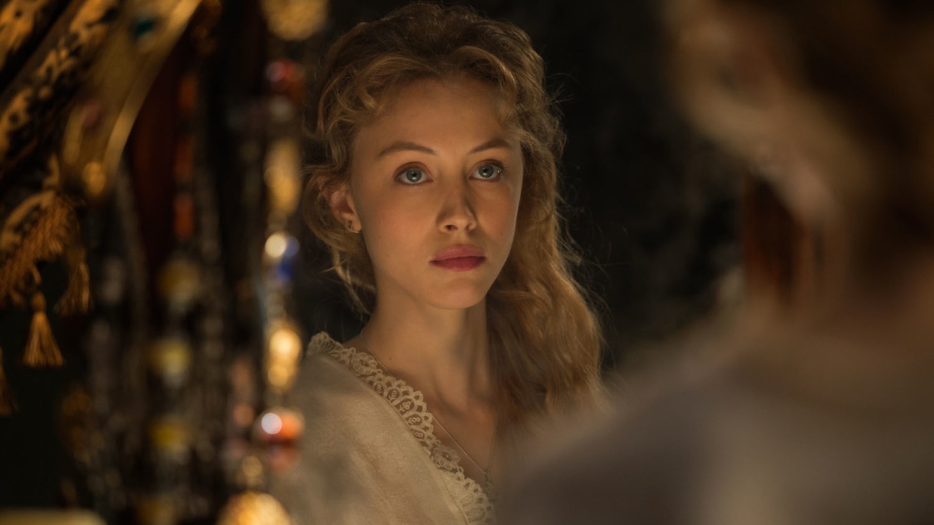 A high-definition desktop wallpaper featuring a scene from the movie Dracula Untold, showing a woman with long, wavy hair gazing intently, illuminated by warm, soft light.