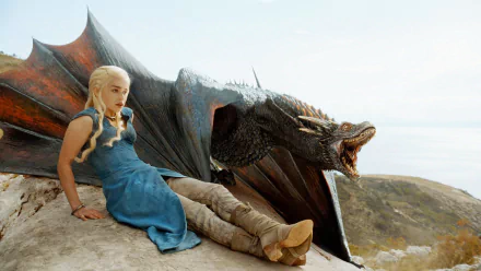 HD wallpaper featuring Emilia Clarke as Daenerys Targaryen from Game of Thrones, sitting beside a dragon against a scenic backdrop.