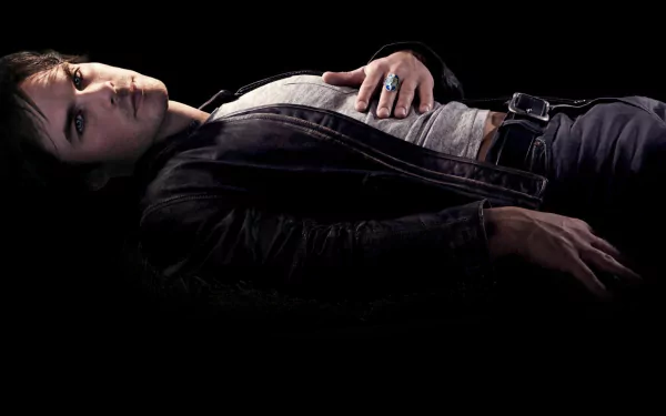 A dramatic HD wallpaper from The Vampire Diaries, featuring a character lying down against a dark backdrop, exuding a mysterious and moody atmosphere.