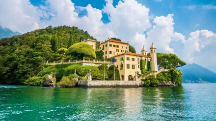 HD desktop wallpaper featuring Villa Balbianello, a man-made architectural gem surrounded by lush trees and a serene lake under a bright blue sky.