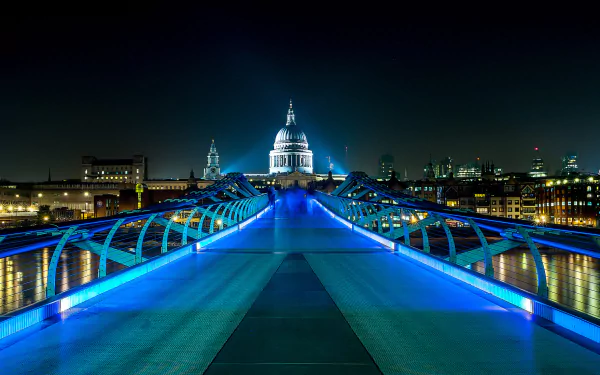 Night view of the illuminated Millennium Bridge in London, England, showcasing its modern design and bright lights leading towards St. Paul's Cathedral, captured in HD.