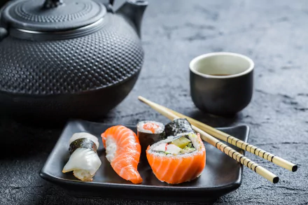 A 4K Ultra HD desktop wallpaper featuring sushi pieces, a black teapot, a small cup of tea, and chopsticks on a textured gray surface.
